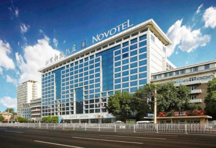 Exterior of Novotel Beijing Xinqiao, a gay-friendly hotel in Beijing. Modern building with blue glass windows under a bright sky.