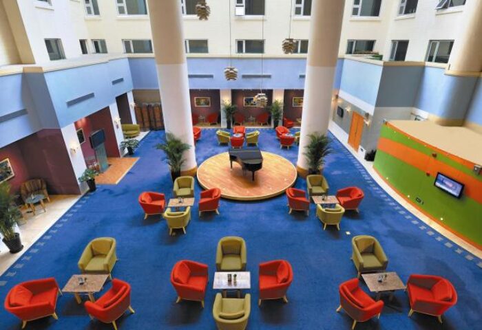 Novotel Beijing Xinqiao interior. Gay-friendly hotel with a piano on a stage, surrounded by colorful seating areas. Modern design.