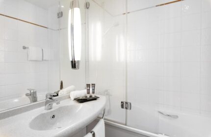Bathroom at gay-friendly Novotel Budapest Centrum Hotel. Features a sink, mirror, toiletries, and a glass-enclosed shower/tub. Modern design.