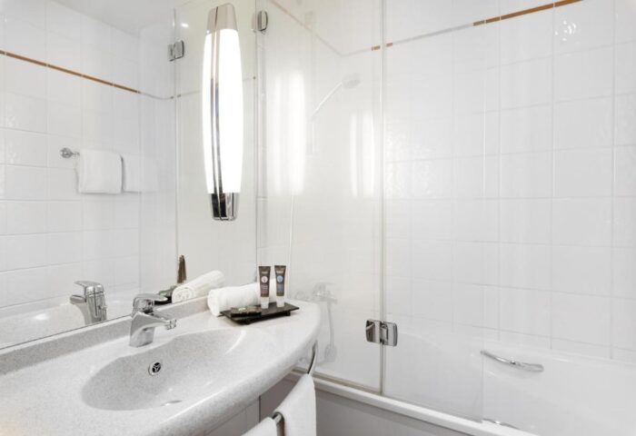 Bathroom at gay-friendly Novotel Budapest Centrum Hotel. Features a sink, mirror, toiletries, and a glass-enclosed shower/tub. Modern design.