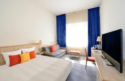 Novotel Budapest Centrum Hotel room. Modern interior with bed, sofa, TV, blue curtains. Gay-friendly hotel in Budapest, Hungary.