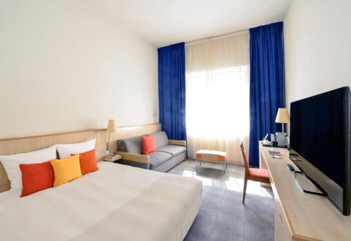 Novotel Budapest Centrum Hotel room. Modern interior with bed, sofa, TV, blue curtains. Gay-friendly hotel in Budapest, Hungary.
