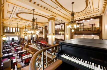 Elegant dining room at the gay-friendly Novotel Budapest Centrum Hotel. Grand piano, chandeliers, and ornate ceiling details create a luxurious ambiance.