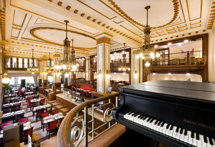 Elegant dining room at the gay-friendly Novotel Budapest Centrum Hotel. Grand piano, chandeliers, and ornate ceiling details create a luxurious ambiance.