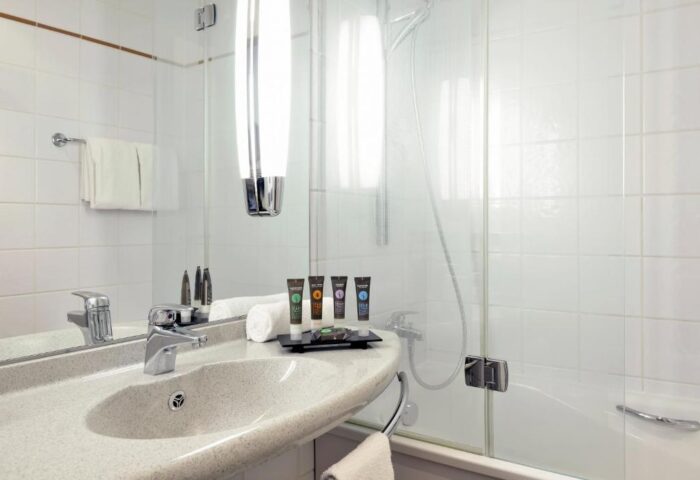 Bathroom at Novotel Budapest Centrum Hotel, a gay-friendly hotel. Sink, amenities, shower, and white tiles. Ideal for gay travel in Budapest.