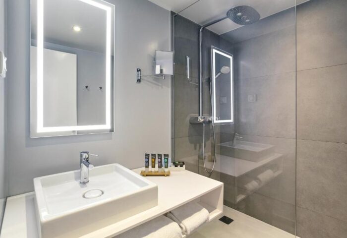 Bathroom at Novotel London Waterloo Hotel, a gay-friendly hotel. Features a sink, lighted mirror, and shower with glass door. Modern design.