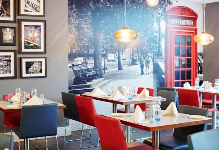 Dining area at Novotel London Waterloo Hotel. Gay-friendly hotel with London themed decor, including a red telephone box mural. Tables set for dining.