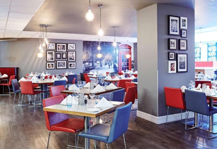 Novotel London Waterloo Hotel restaurant. Tables set, red & blue chairs. Gay-friendly hotel dining with London phone booth mural.