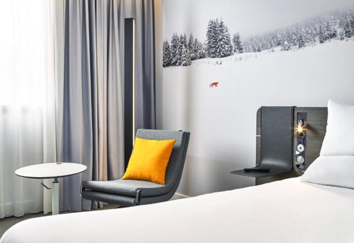 Novotel London Waterloo Hotel room. Modern decor, chair with yellow pillow, winter scene wall art. Gay-friendly hotel room interior.