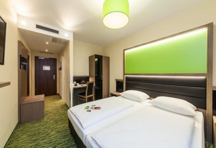 Novum Hotel Aldea Berlin Zentrum gay-friendly room. Double bed, desk, and green accents. Modern design for a comfortable stay in Berlin.