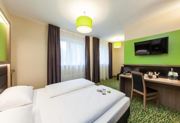 Novum Hotel Aldea Berlin Zentrum room. Gay-friendly hotel with bed, desk, TV, and green accents. Modern design for gay travelers in Berlin.