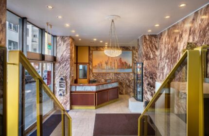 Novum Hotel Leonet Köln Altstadt lobby. Gay-friendly hotel with marble walls, chandelier, and city skyline art. Stairs with gold railings.