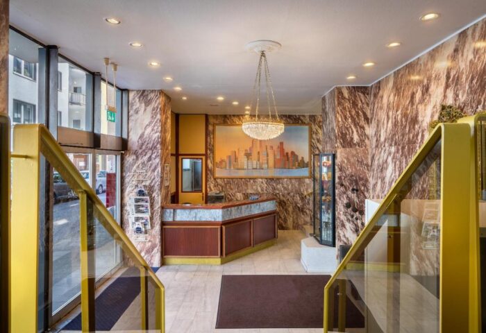 Novum Hotel Leonet Köln Altstadt lobby. Gay-friendly hotel with marble walls, chandelier, and city skyline art. Stairs with gold railings.