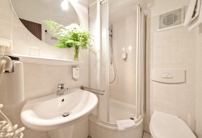 Bathroom at Novum Hotel Leonet Köln Altstadt, a gay-friendly hotel. Sink, shower, toilet, mirror, and fresh flowers. Clean and modern.