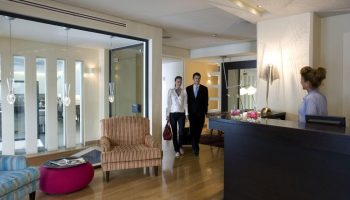 O&B Athens Boutique Hotel lobby. Guests checking in at this gay-friendly hotel. Modern interior design, wooden floors, and reception desk.