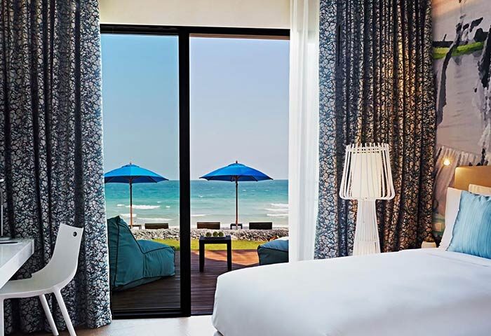 OZO Chaweng Samui gay-friendly hotel room with ocean view. Beach umbrellas, seating, and a glimpse of the sea visible from the balcony.