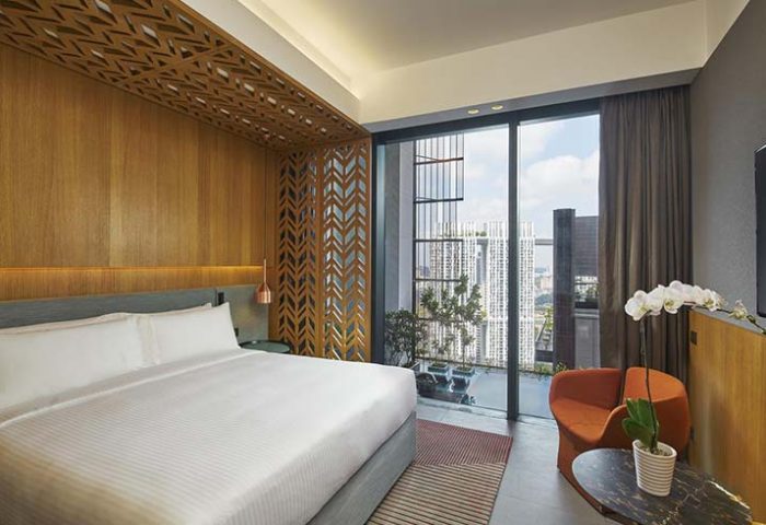 Oasia Hotel Downtown Singapore room. Gay-friendly hotel with a bed, chair, and city view. Far East Hospitality offers luxury.
