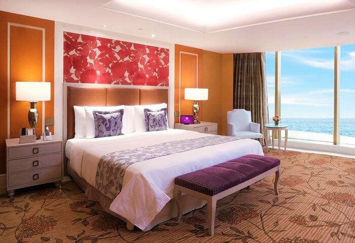 Okada Manila gay-friendly hotel room. Luxurious bedroom with ocean view, king-size bed, and purple accents. Upscale travel for gay men.