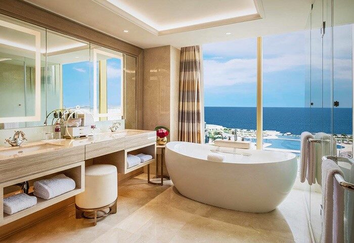 Okada Manila gay-friendly hotel bathroom. Bathtub overlooking ocean. Double sink vanity, stool, and towels. Luxury travel for gay men.