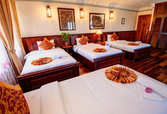 Okay Boutique Hotel gay-friendly room. Four single beds with white linens, decorative pillows, and towels. Wooden furniture, warm lighting.