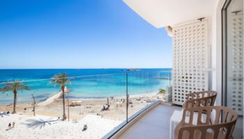 Balcony view from One Ibiza Suites, a gay-friendly hotel. Beach, turquoise sea, and palm trees. Perfect for gay men's travel to Ibiza.