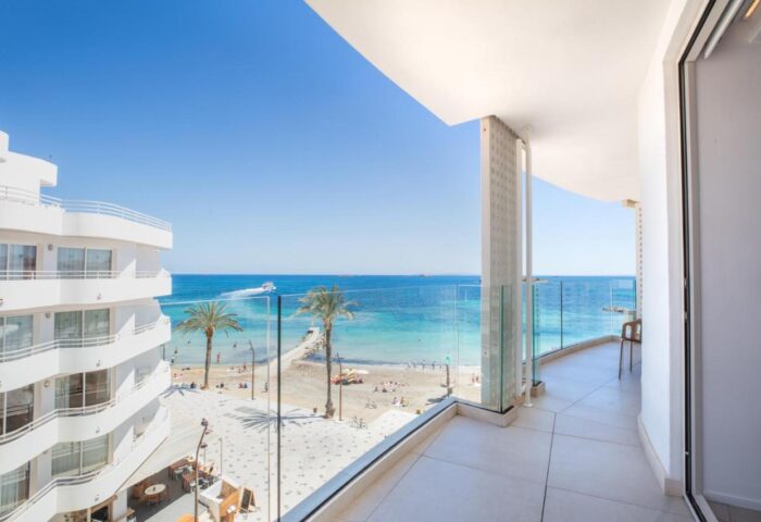 View from One Ibiza Suites, a gay-friendly hotel. Balcony overlooking the beach, palm trees, and blue sea. Perfect for gay travel in Ibiza.