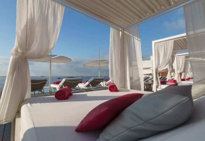 Gay-Friendly One Ibiza Suites: Luxurious daybeds with white canopies, pink accents, and ocean views. Perfect for relaxing at this Ibiza hotel.