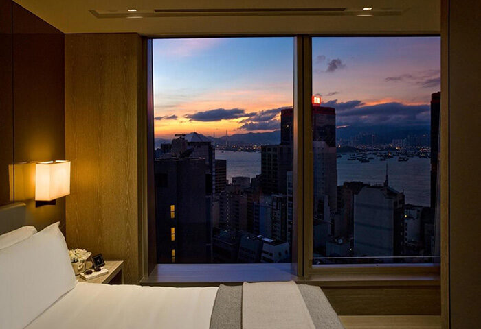 One96, gay-friendly hotel room view at dusk. Skyline with sea, buildings, and colorful sky seen from the window. Modern, upscale lodging.