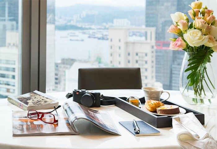 One96, gay-friendly hotel. Table setting with camera, flowers, breakfast tray, city view. Gay travel luxury and comfort.