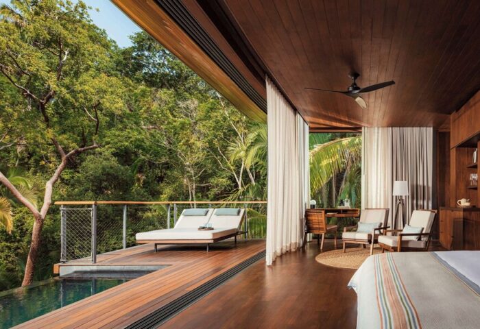 One&Only Mandarina gay-friendly hotel suite. Deck with loungers overlooks a pool and lush jungle. Interior with desk, chairs, and wood accents.