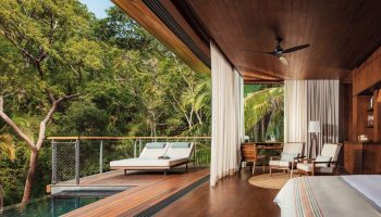 One&Only Mandarina gay-friendly hotel suite. Deck with loungers overlooks a pool and lush jungle. Interior with desk, chairs, and wood accents.