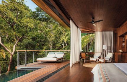 One&Only Mandarina gay-friendly hotel suite. Deck with loungers overlooks a pool and lush jungle. Interior with desk, chairs, and wood accents.
