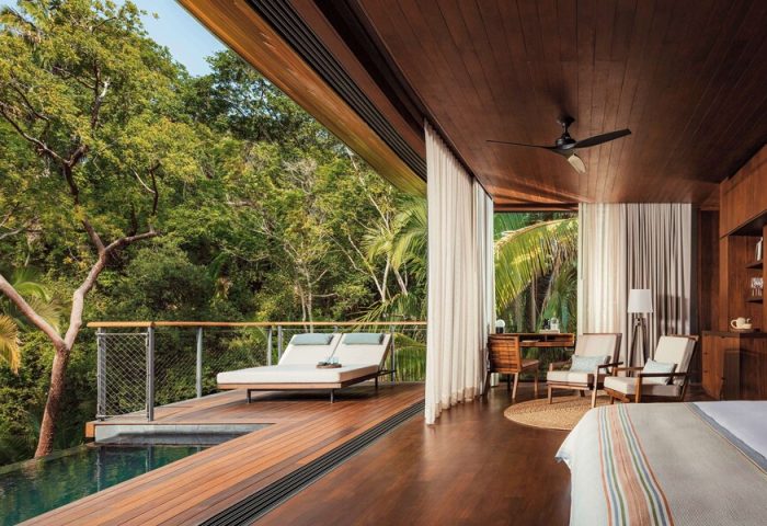 One&Only Mandarina gay-friendly hotel suite. Deck with loungers overlooks a pool and lush jungle. Interior with desk, chairs, and wood accents.
