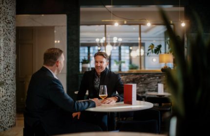 Two men chatting at a table in the stylish lounge of the gay-friendly Opus Hotel. The hotel offers a welcoming and inclusive atmosphere for gay travelers.