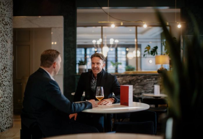 Two men chatting at a table in the stylish lounge of the gay-friendly Opus Hotel. The hotel offers a welcoming and inclusive atmosphere for gay travelers.