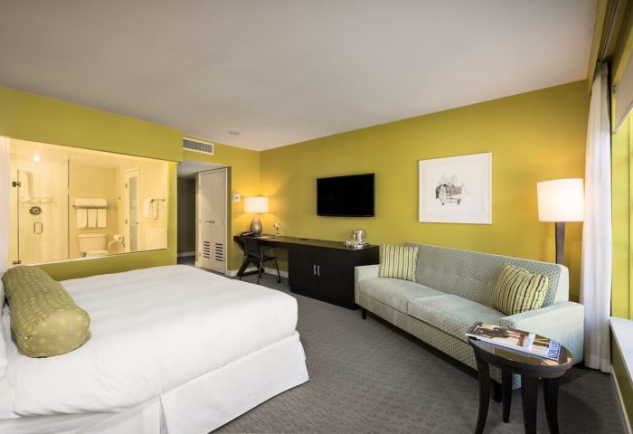 Opus Hotel room. Gay-friendly hotel with a bed, sofa, desk, and a bathroom with a glass wall. Modern design with yellow walls.