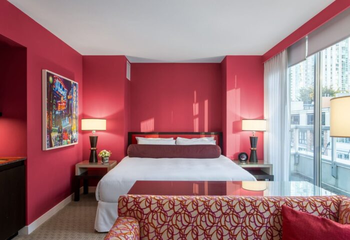 Opus Hotel room with red walls. Gay-friendly hotel with modern design. A luxurious bedroom with a king bed, lamps, and a city view.