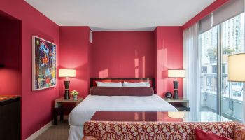 Opus Hotel room with red walls. Gay-friendly hotel with modern design. A luxurious bedroom with a king bed, lamps, and a city view.