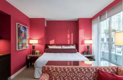 Opus Hotel room with red walls. Gay-friendly hotel with modern design. A luxurious bedroom with a king bed, lamps, and a city view.