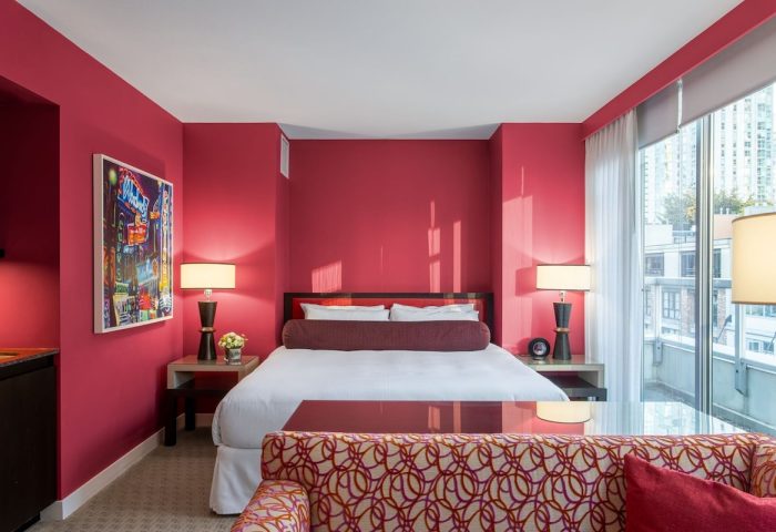 Opus Hotel room with red walls. Gay-friendly hotel with modern design. A luxurious bedroom with a king bed, lamps, and a city view.