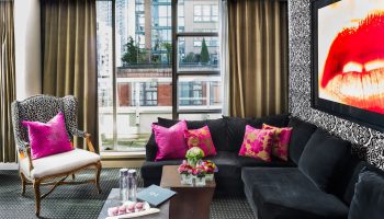 Opus Hotel room. Gay-friendly hotel interior with a black couch, bright pink pillows, and a city view. Modern design for gay men travel.