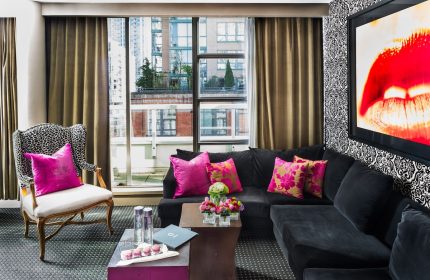 Opus Hotel room. Gay-friendly hotel interior with a black couch, bright pink pillows, and a city view. Modern design for gay men travel.