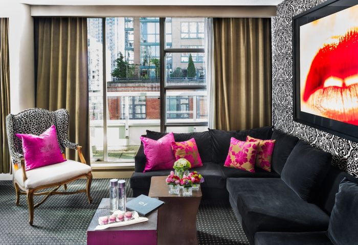 Opus Hotel room. Gay-friendly hotel interior with a black couch, bright pink pillows, and a city view. Modern design for gay men travel.