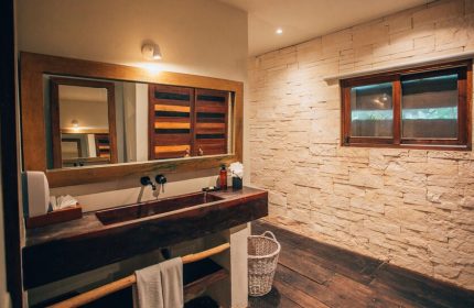 Orchid Beach House Adults Only bathroom. Rustic wood sink, stone wall, window. Gay-friendly hotel design.