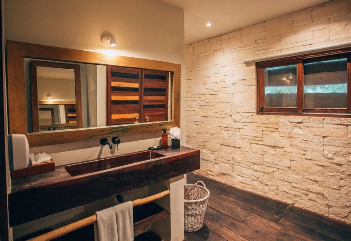 Orchid Beach House Adults Only bathroom. Rustic wood sink, stone wall, window. Gay-friendly hotel design.