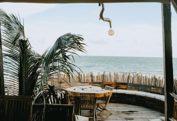 Orchid Beach House Adults Only, gay-friendly hotel. Ocean view from a wooden deck with table, chairs, and palm tree. Relaxing tropical vibe.