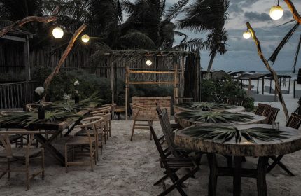 Orchid Beach House Adults Only gay-friendly hotel outdoor dining area. Tables on the sand, palm trees, and string lights.