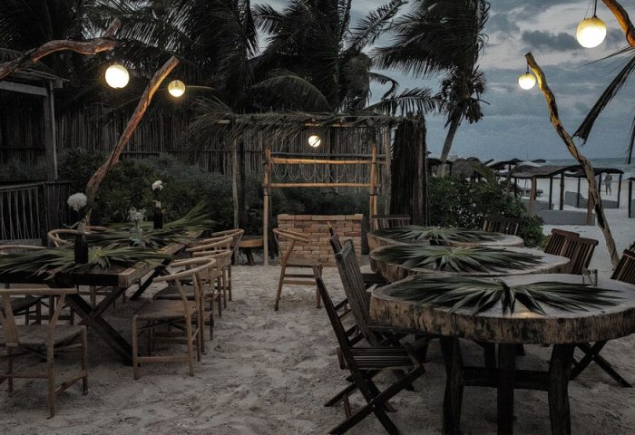 Orchid Beach House Adults Only gay-friendly hotel outdoor dining area. Tables on the sand, palm trees, and string lights.