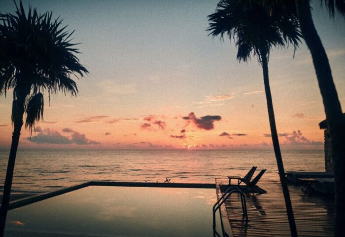 Our Habitas Tulum gay-friendly hotel sunset view. Oceanfront pool with palm trees. Relaxing gay travel destination.