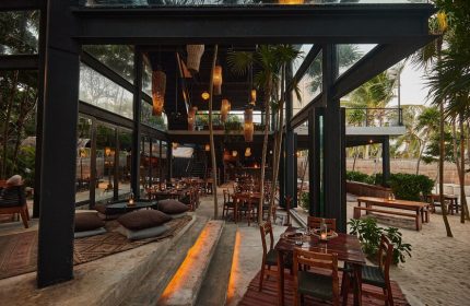 Our Habitas Tulum gay-friendly hotel dining area. Open-air restaurant with wooden tables, pillows, and woven light fixtures.